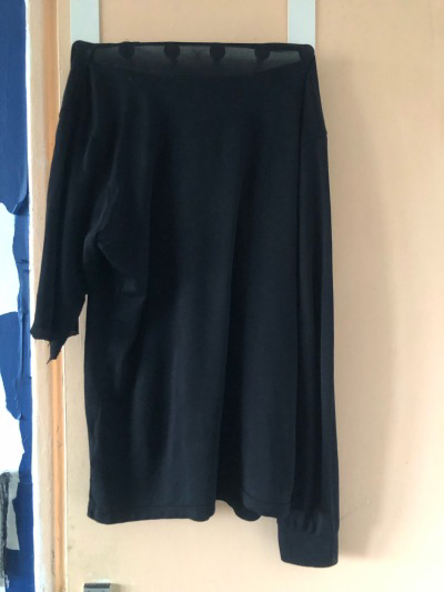 a black top hung out to launder on the back of a door over a 6 pegs of an over door hook. the sleeve was trapped in the washing machine door and ripped off from the elbow