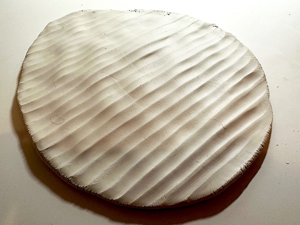 When flattening the clay, I pressed my palm into the surface with my body weight, and the clay yielded, retaining the soft imprint of my hand. After turning it over and drawing lines with my fingers on the uneven surface, the lines emerged as gentle waves, shaped by the clay’s own undulations rather than by my original intention. During making, cracks appeared along the edges, introducing an unforeseen transformation generated by the material itself.