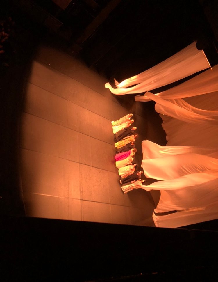 Curtain call for a theatre performance with flowing white draping set behind the performers, with wind blowing the set.