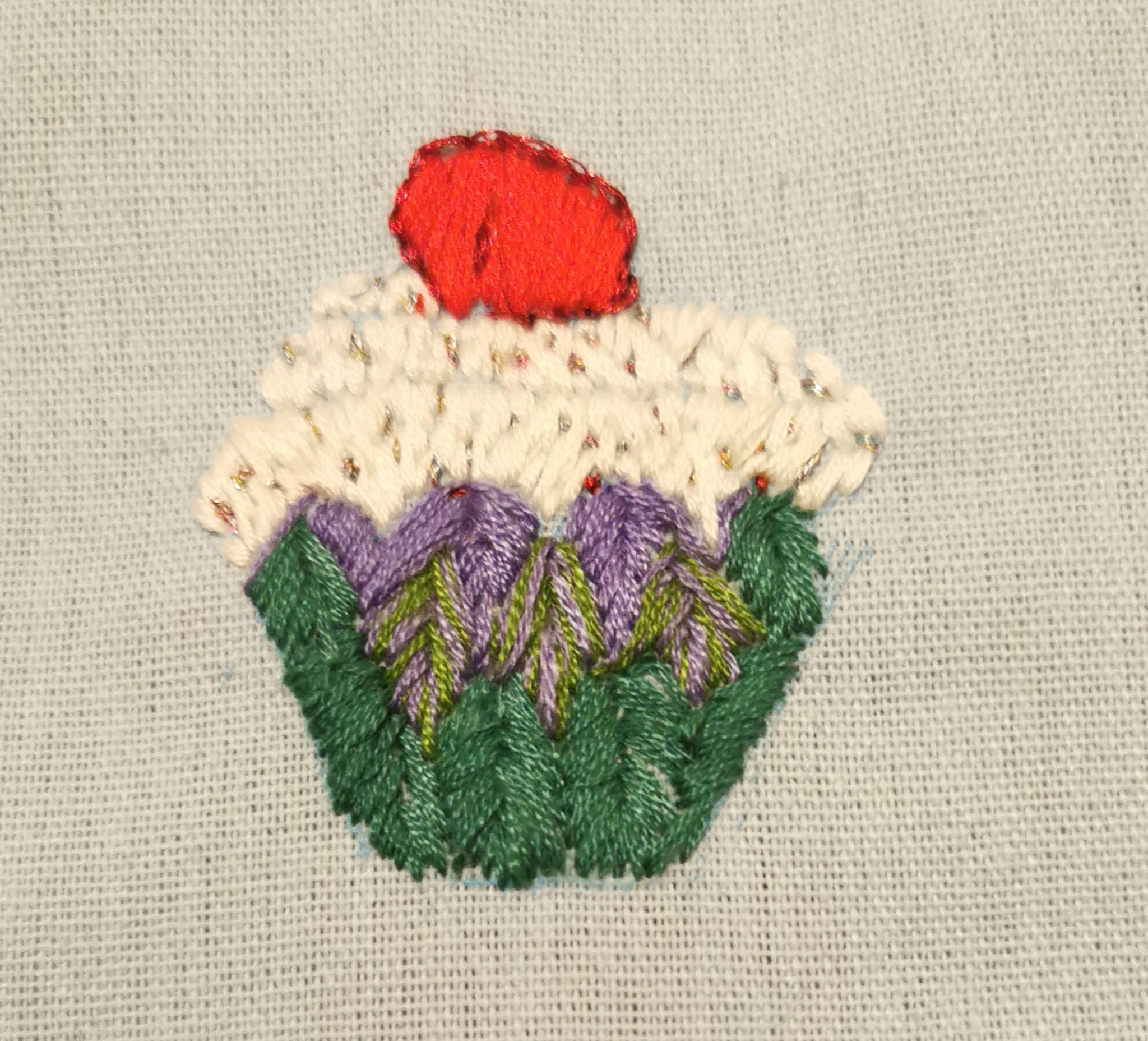 Embroidered cupcake, Different coloured thread and stiches. Red cherry, white and glittery icing, Green heron stitch cupcake case.