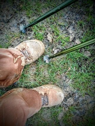 Photograph of muddy shoes, trouser bottoms and ends of walking poles