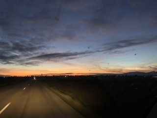 Photo taken by car, we see the road and the white line in perspective, advancing towards a pink horizon, blue white gray, it's evening falling