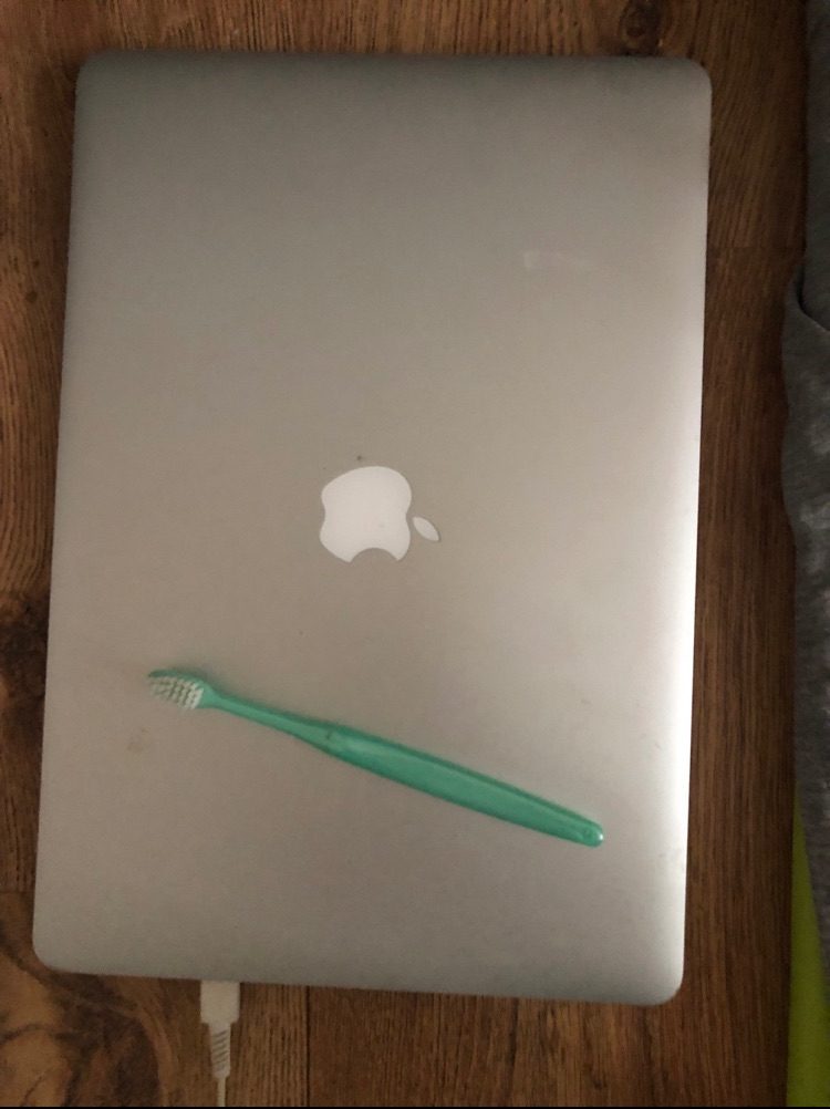 a pearlescent green toothbrush on top of a closed silver laptop. Photographed flatly and above
