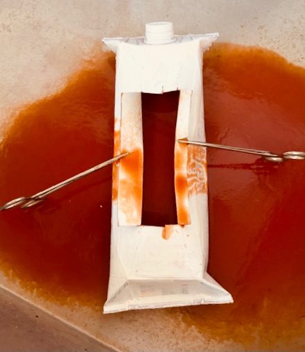 video still of a tetrapak of tomato juice surgically drained