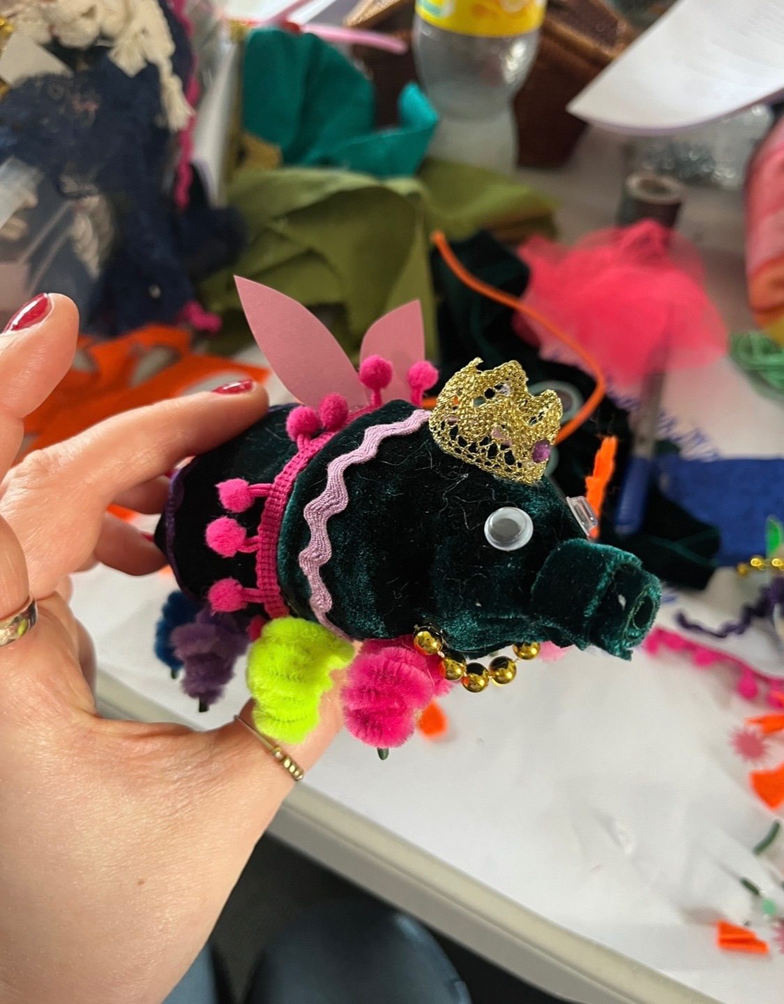 A dark green fabric tardigrade with googly eyes and a tiny tiara