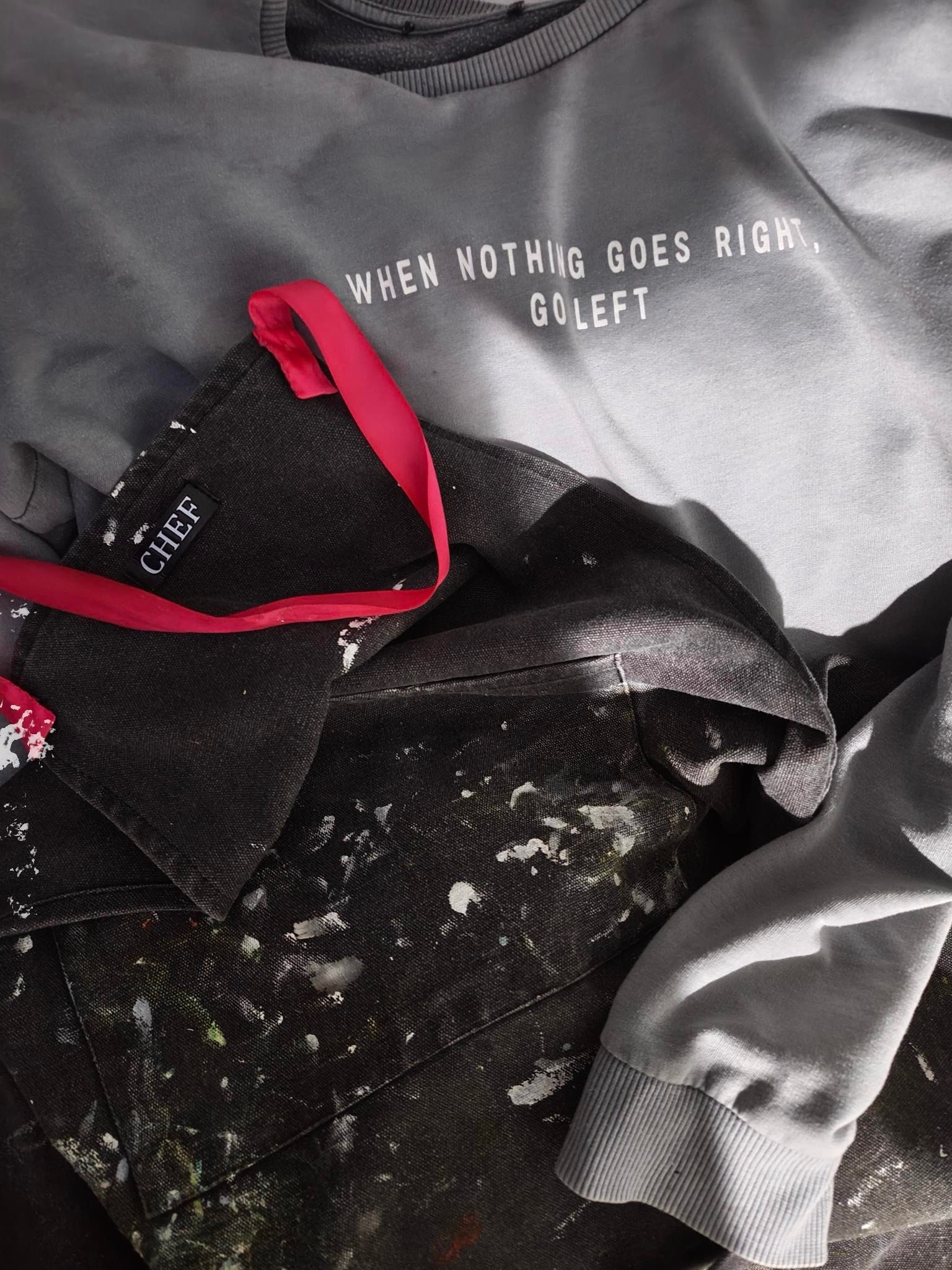 Photo of artists painting outfit waiting to be put on. Track suit with logo, ‘When nothing goes right, go left’ and her apron covered in paint with a small logo saying chef