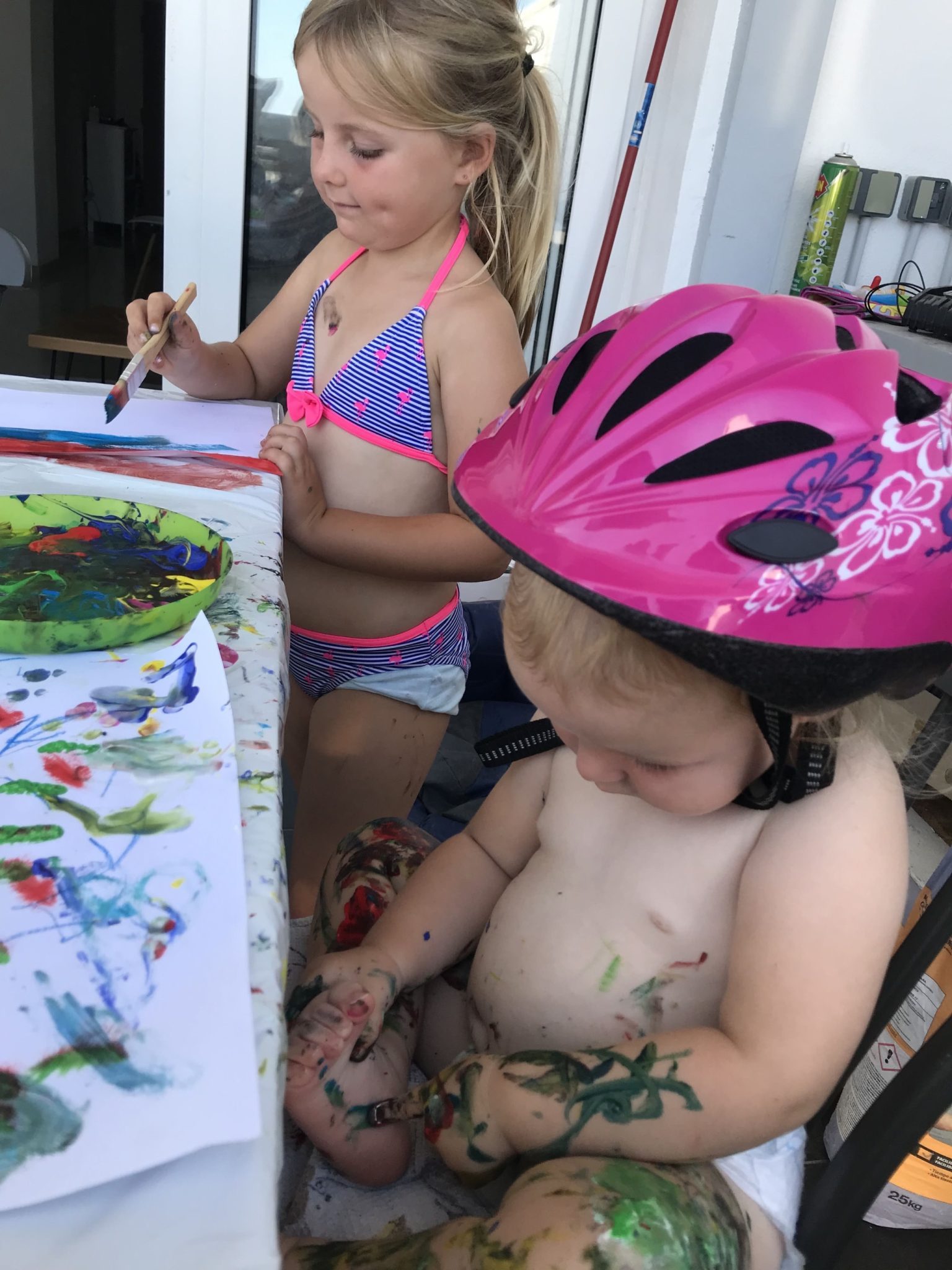Photo of artists grandchildren on a painting day, the youngest who wears a cycle helmet with everything, experimenting with self-painting.