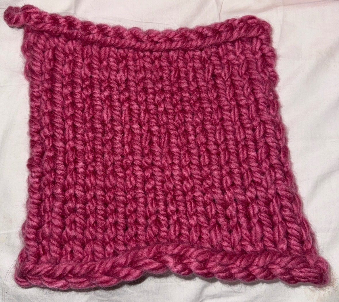 photo of burgundy-ish knit square, very uneven, yet alluring, the border on top is much neater than the starting chain
