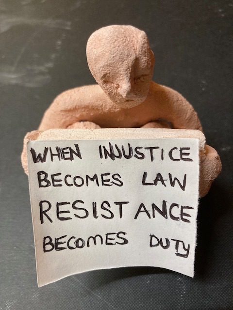 Clay person holds a placard saying when injustice becomes law resistance becomes duty