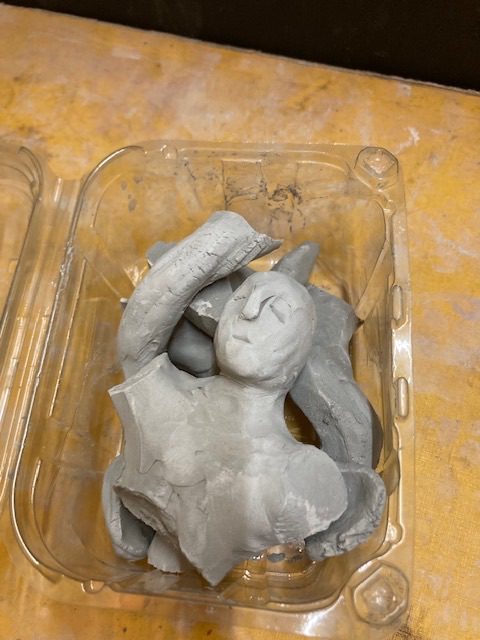 Broken clay person in a single use plastic container