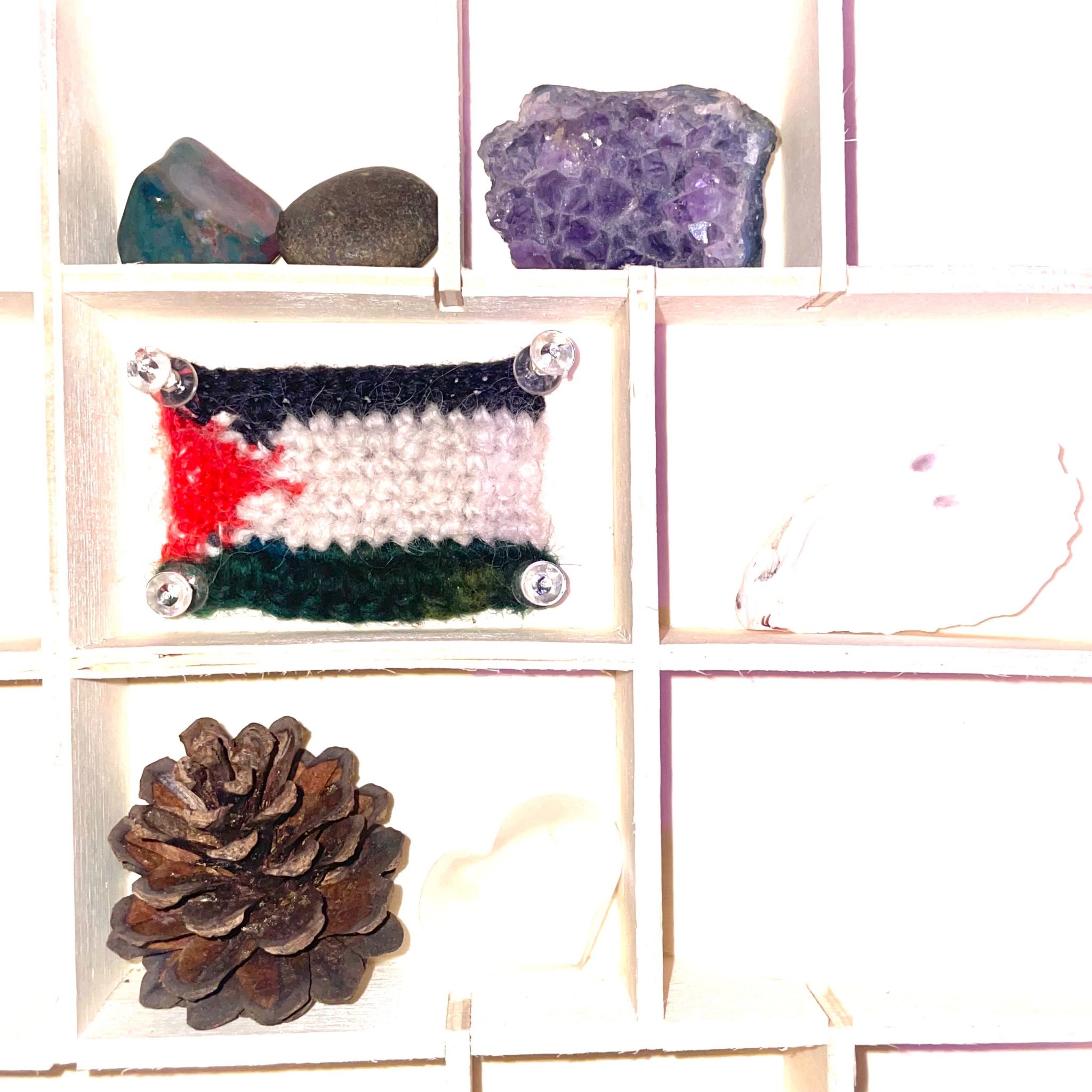 A trinket box holding a pinecone, various crystals including quartz and amethyst, sea glass, shell