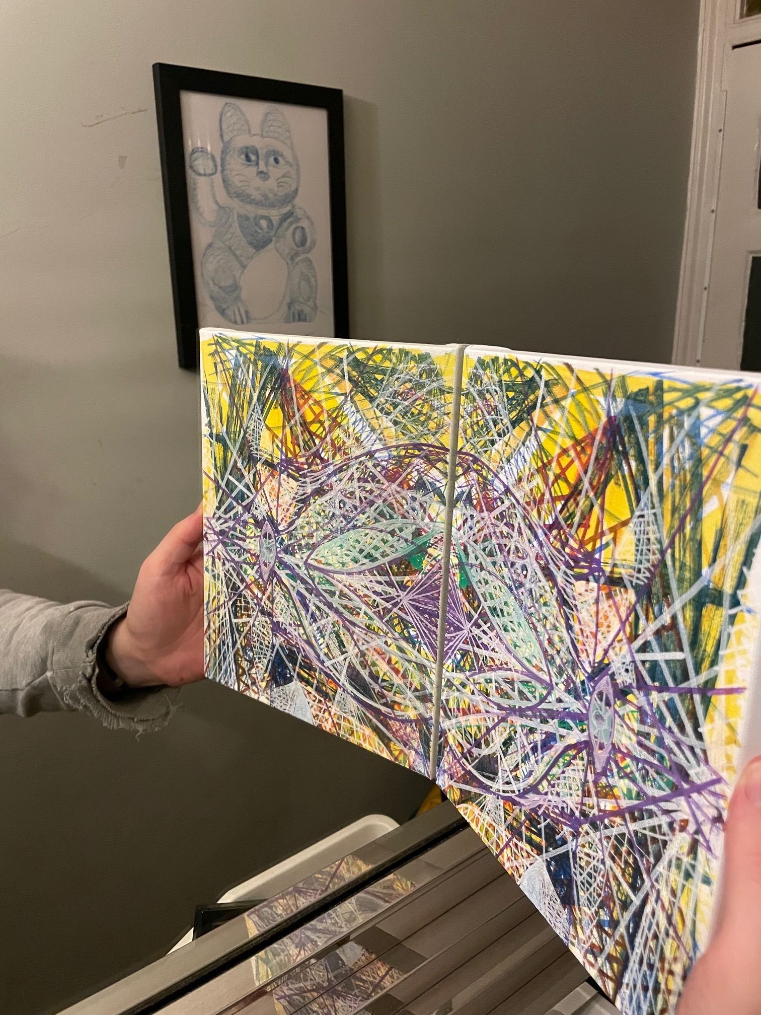 Abstract geometric form with recognisable eye set against a mirror, with a framed lucky cat drawing emerging in the background of the mirror