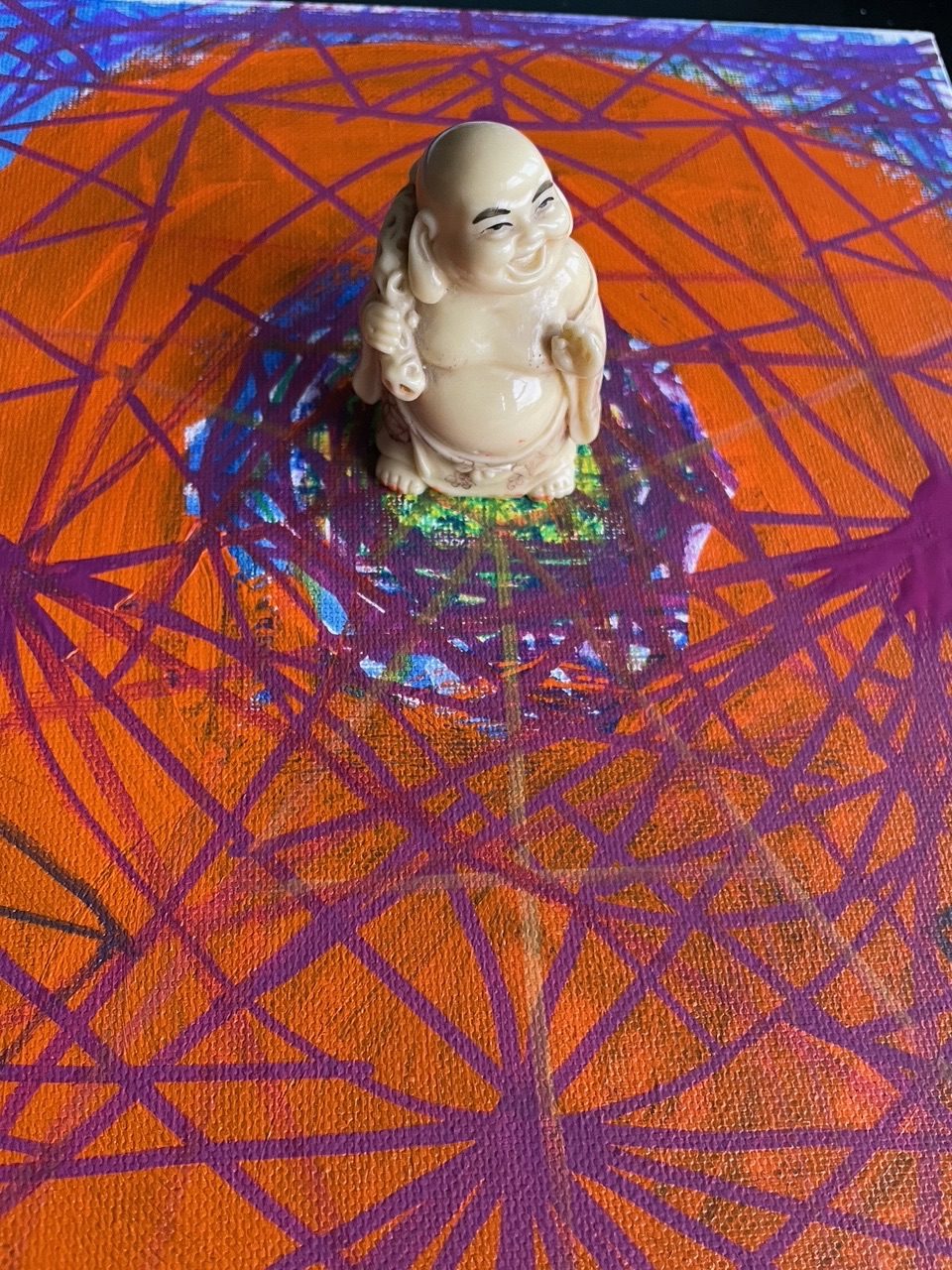 Buddha figurine placed on top of geometric form painted and drawn on canvas with orange and auburn acrylic