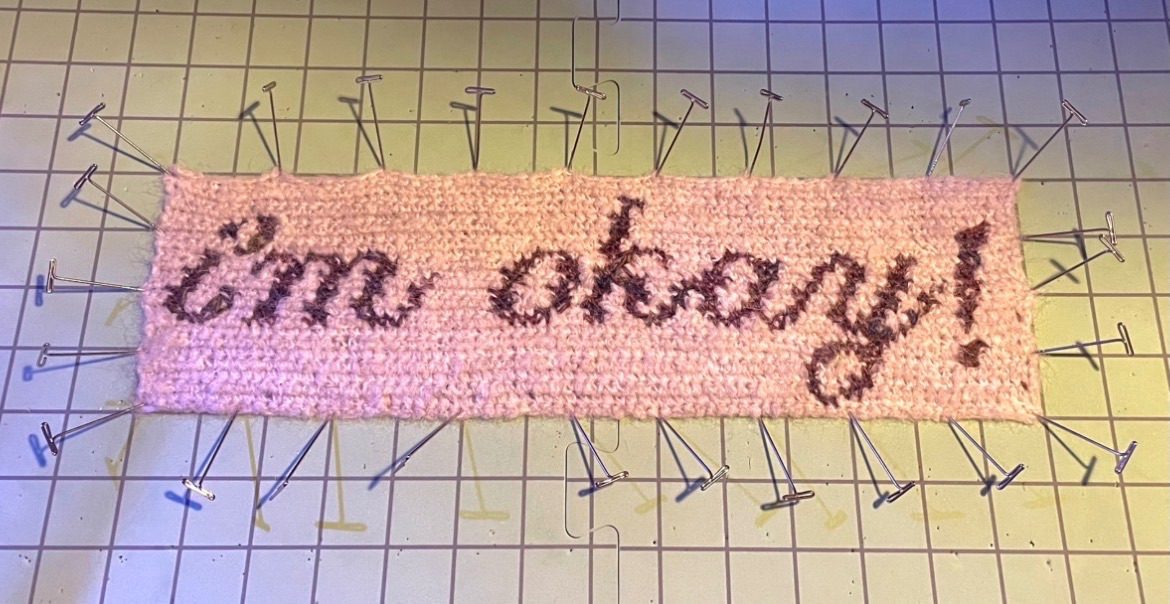 a crocheted tapestry panel with ‘i’m okay!’ written in italic