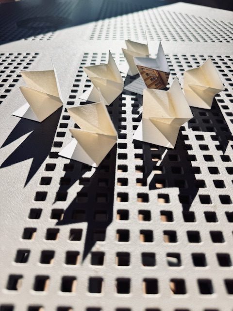 Seven small folded paper sculptures on a metal grid.