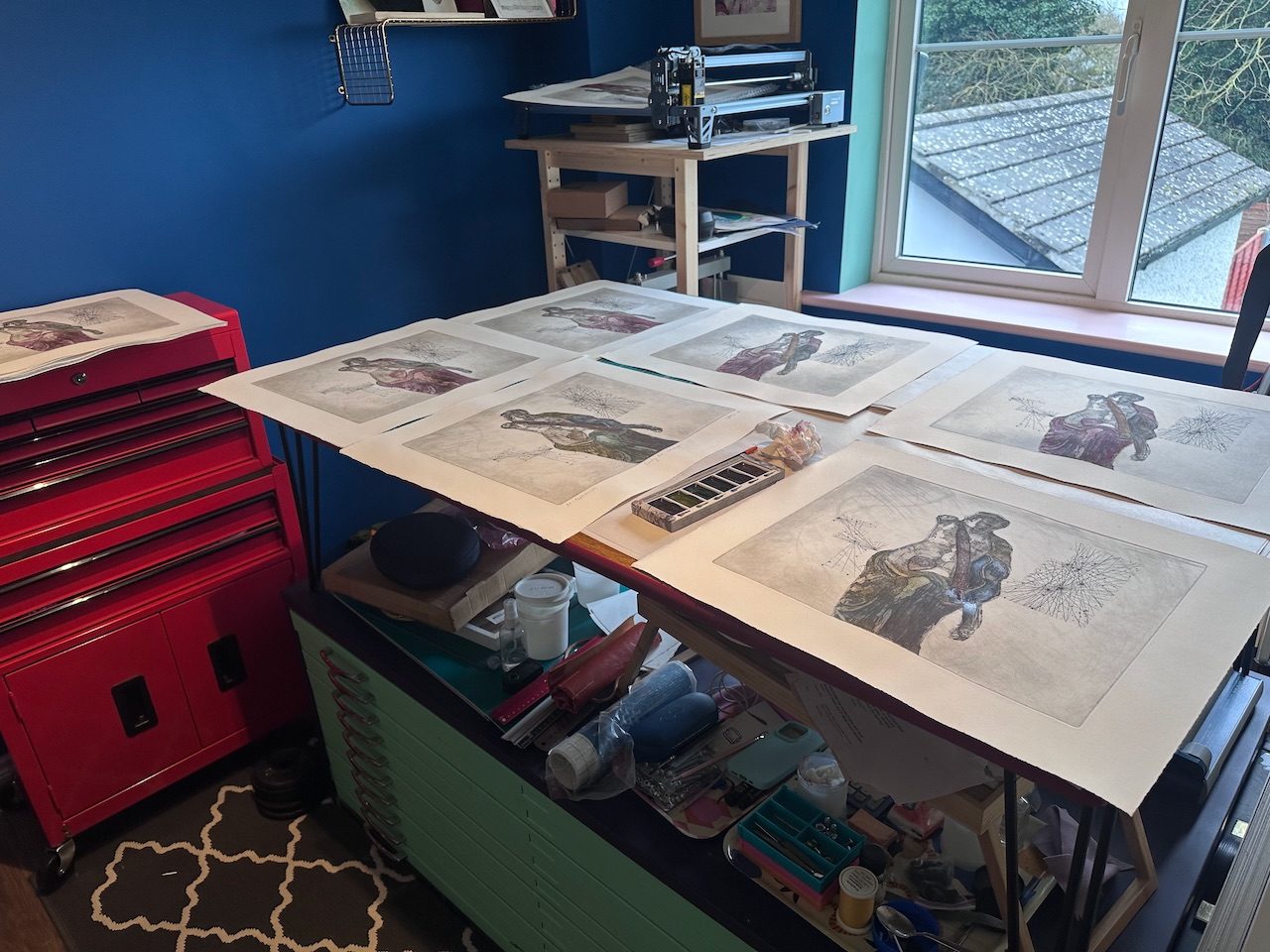 Handcoloured etchings laid out on an art studio table