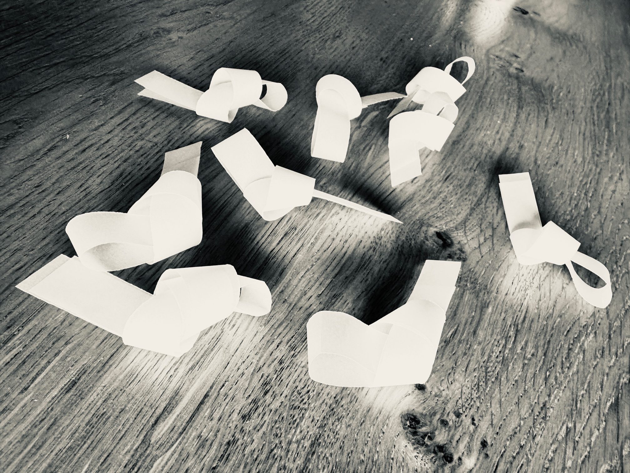 Nine knotted strips of paper sitting together on a wooden surface.