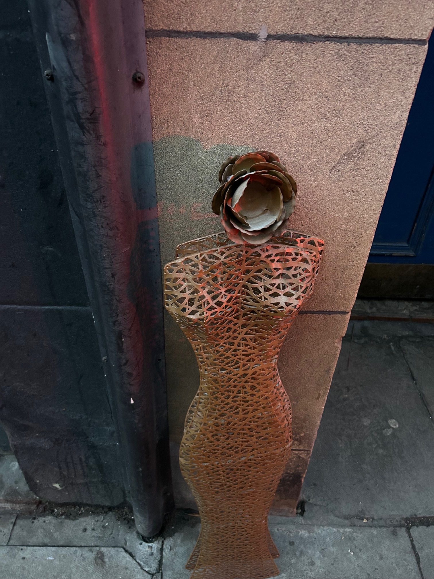 A photograph of a mesh panel in the form of a woman’s dress and with a flower for a head found leaning against a building and since disappeared