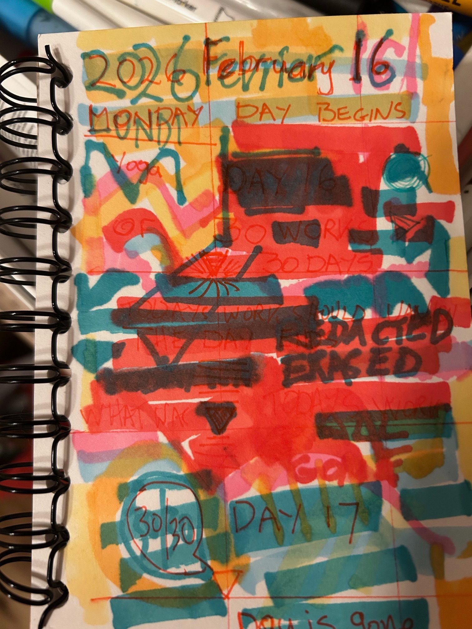 A spiral bound notebook with colour blocking/ redacted text and the day and date written across the top of the page
