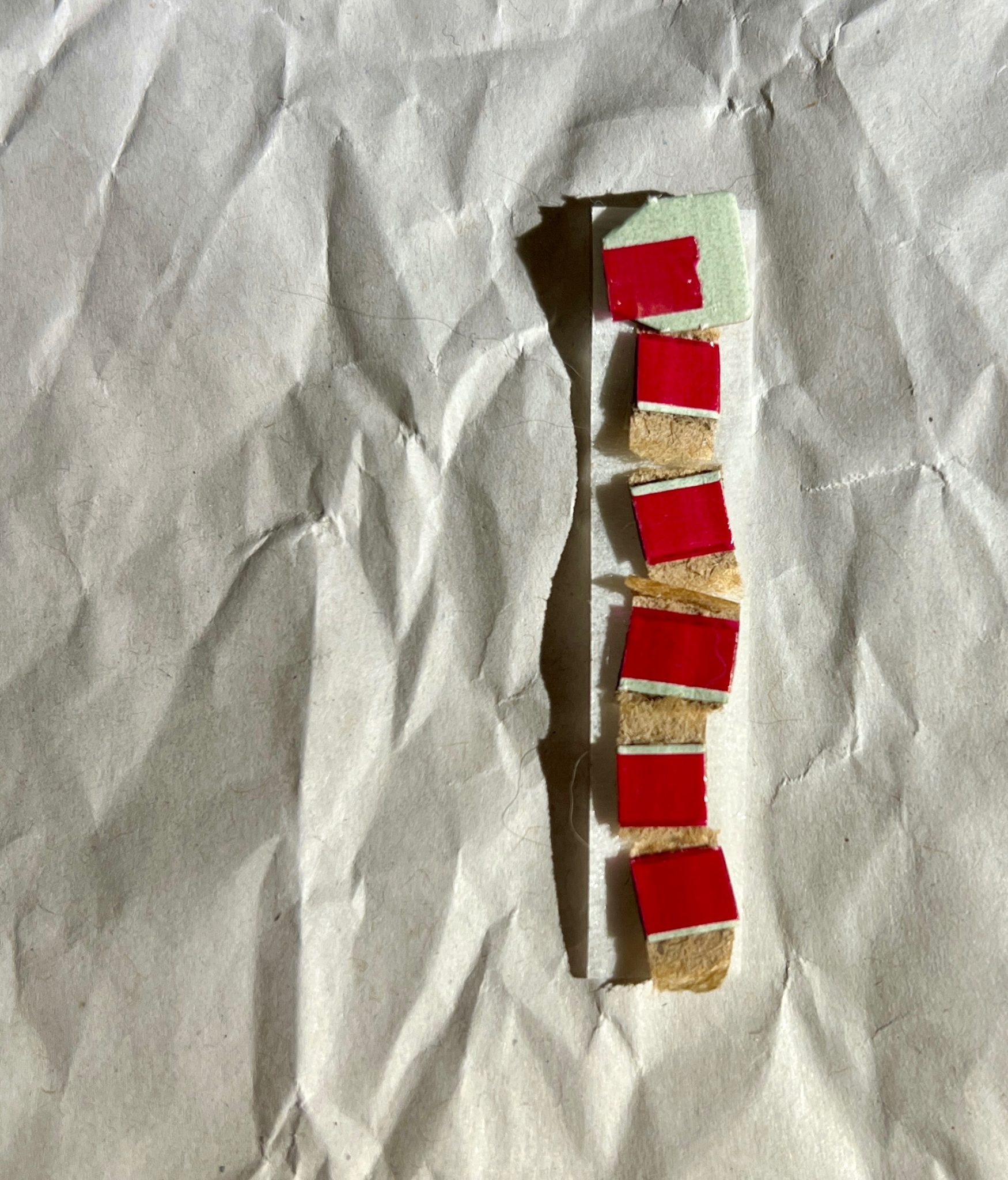 Background - slightly crumpled white paper. Strip of narrow tape to right with six tiny red squares stuck to it.