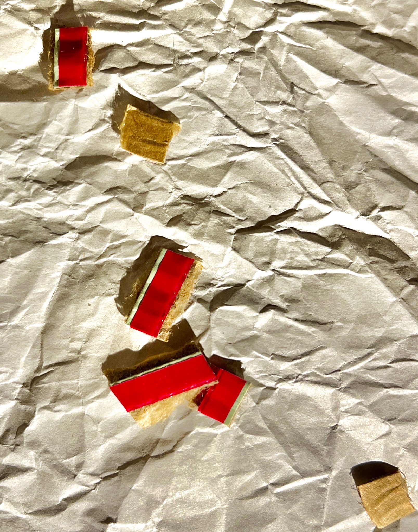 Random pieces of red plastic tear strips from cardboard envelopes on top of crumpled paper. Created with eyes closed.