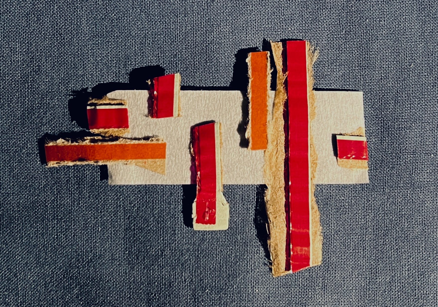 Blue fabric background. Pieces of rip strips from cardboard envelopes, cut to different sizes, stuck to a piece of masking tape.