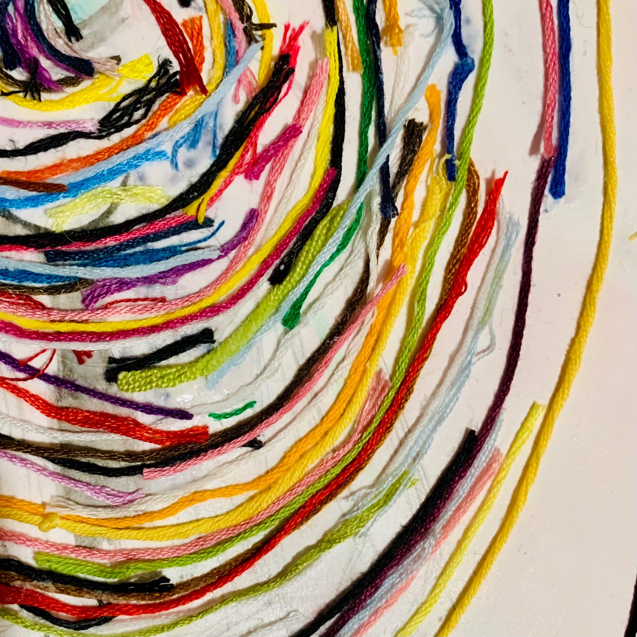 Pieces of embroidery thread glued onto a sketchbook page in a spiral formation