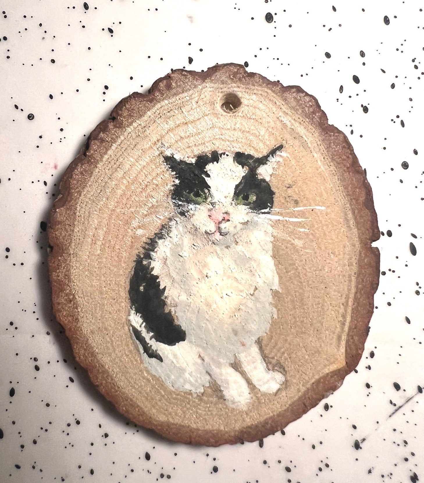 Painting of black and white cat on slice of wood.