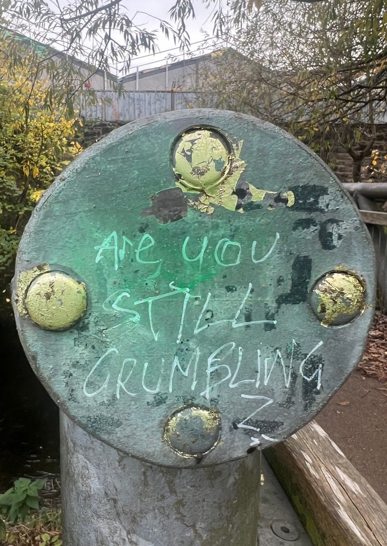 Photograph of graffiti ‘ are you still grumbling’ on bridge across water of Leith.