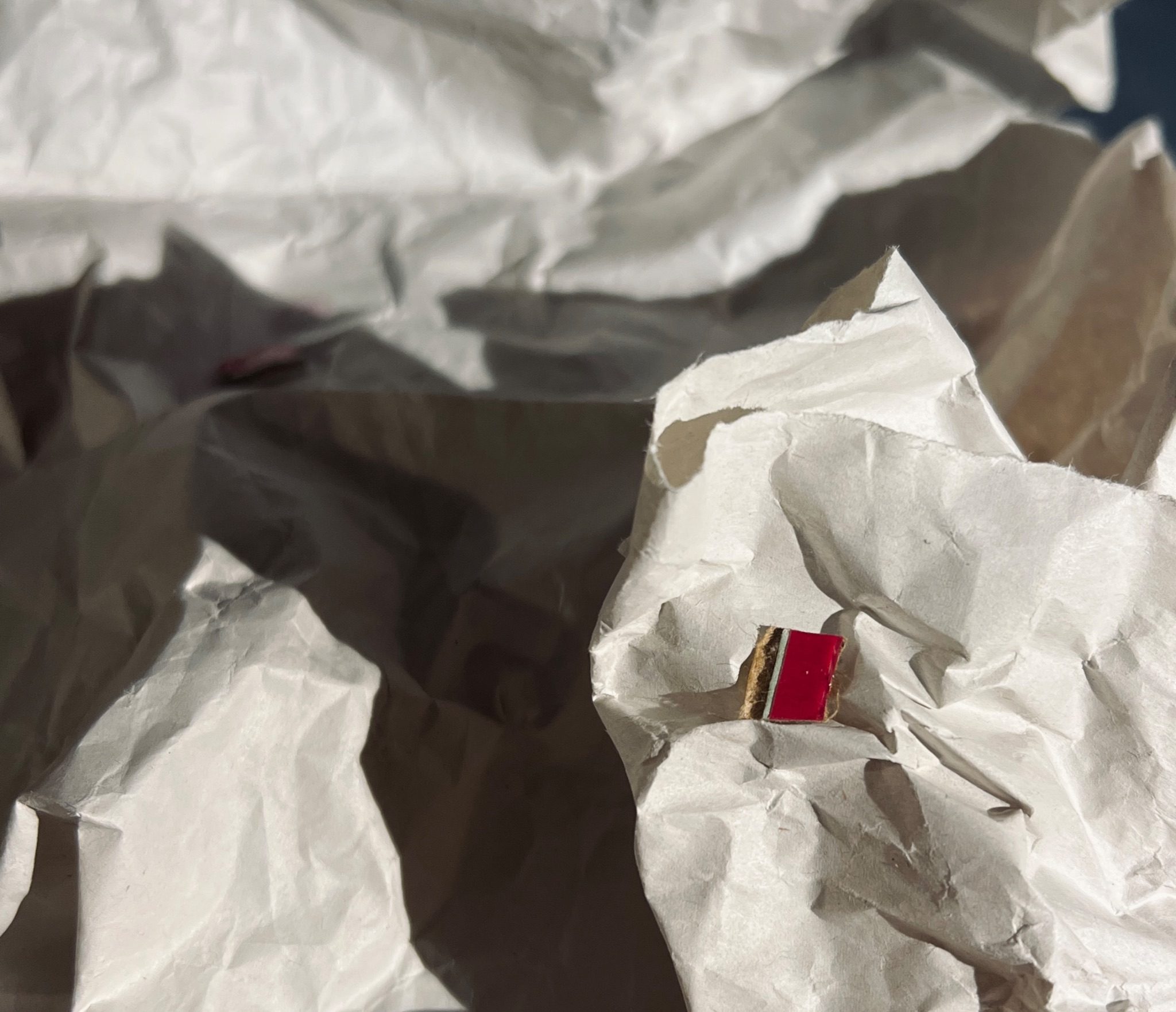 A single scrap of rip-strip from a cardboard envelope balances on some crumpled newsprint paper, with a bright sidelight casting shadows over the paper.