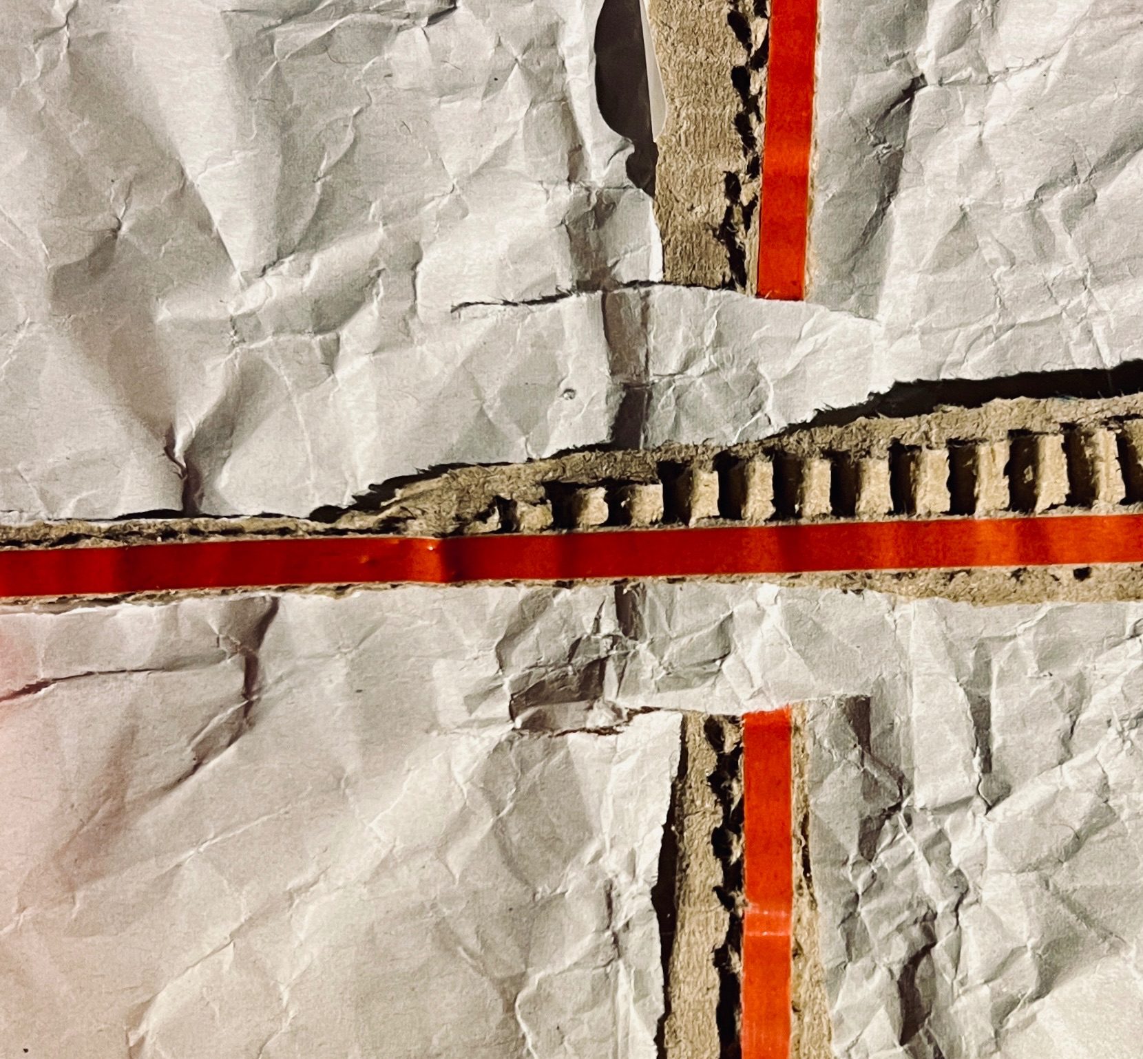 Two pieces of rip-strip from cardboard envelopes lie on a piece of creased paper to form a cross.