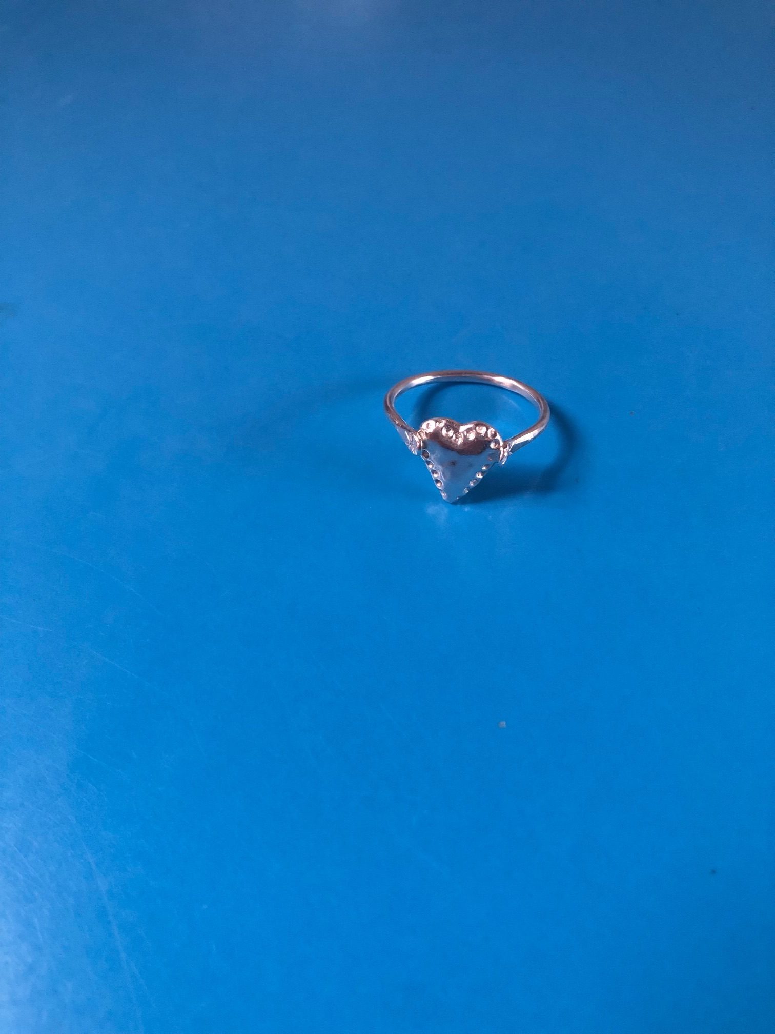 photograph of a heart shaped silver ring on a blue surface