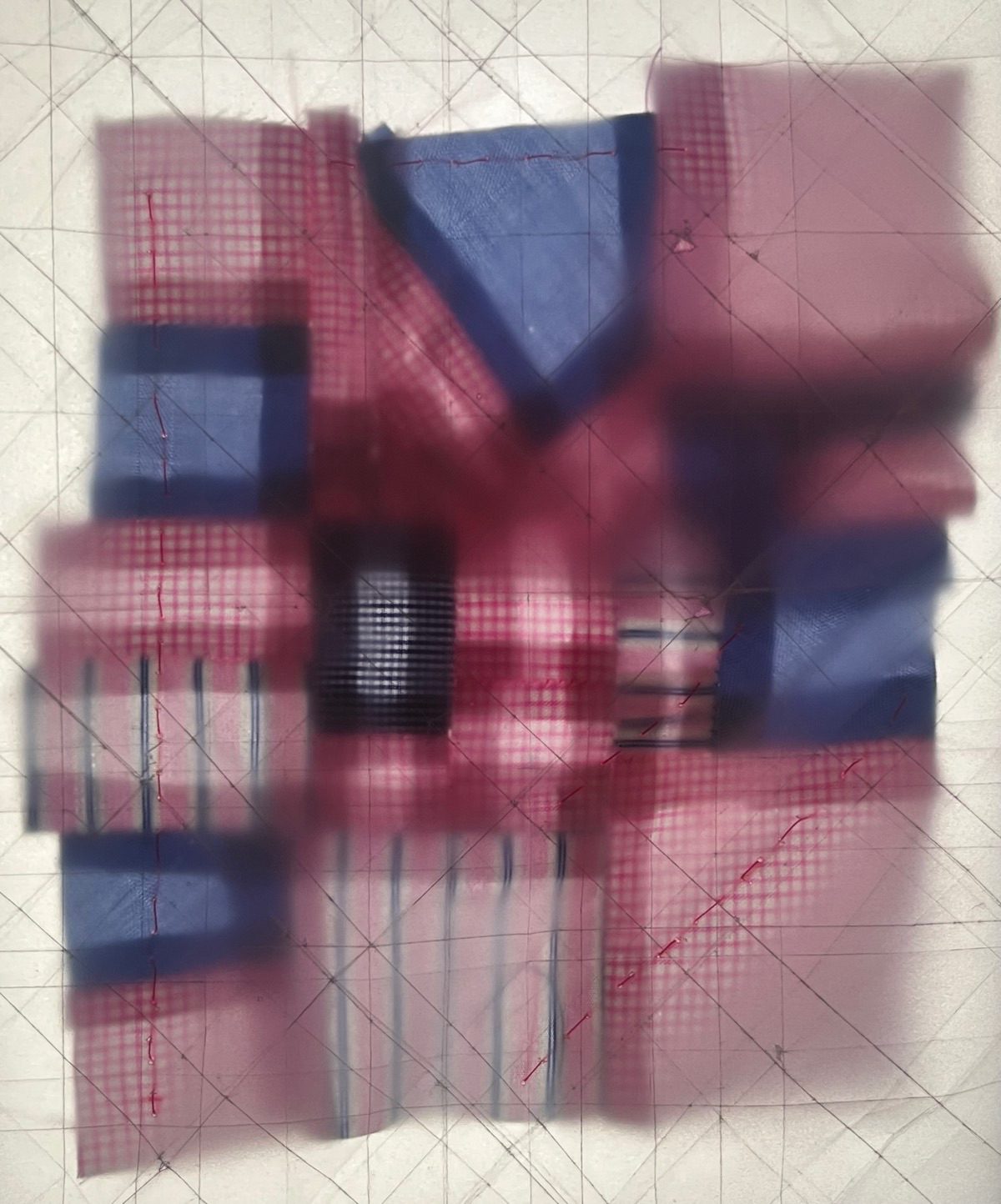 A piece of patchwork fabric made from irregularly sized scraps of cotton office shirts, in shades of pink and blue. A layer of frosted paper with crisp creases is stitched on top of the patchwork, partially blurring some of the fabric.