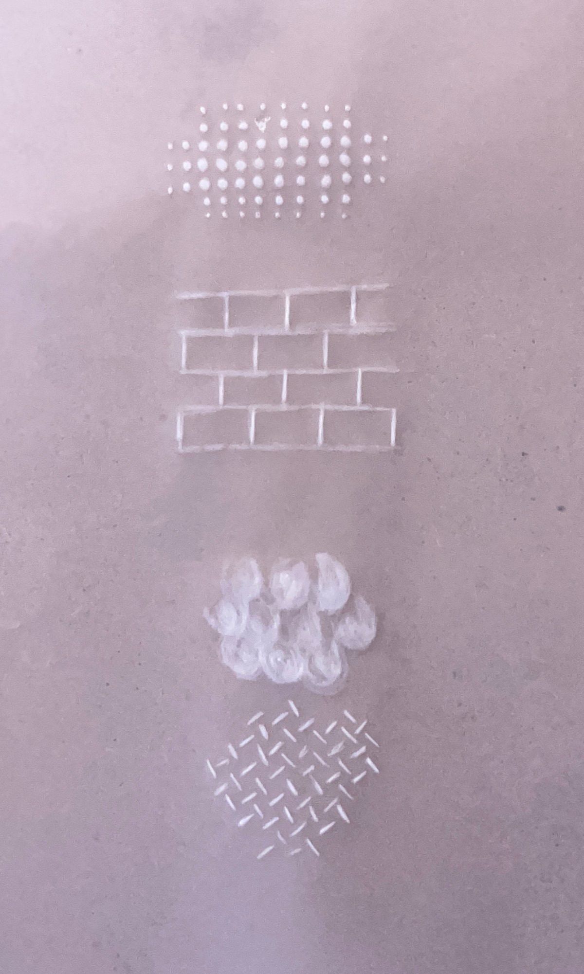 A sheet of tracing paper with four small areas of raised embossing in different patterns. A cluster of evenly spaced dots, a simple brickwork pattern, a group of 5p sized balls, short lines that alternate directions creating a baskweave design.