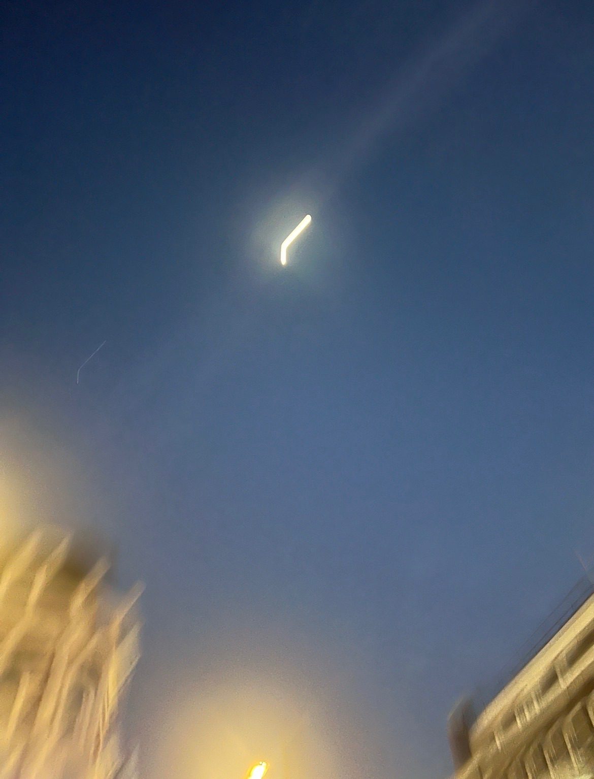 Blurry photo of the first quarter moon above buildings at dusk