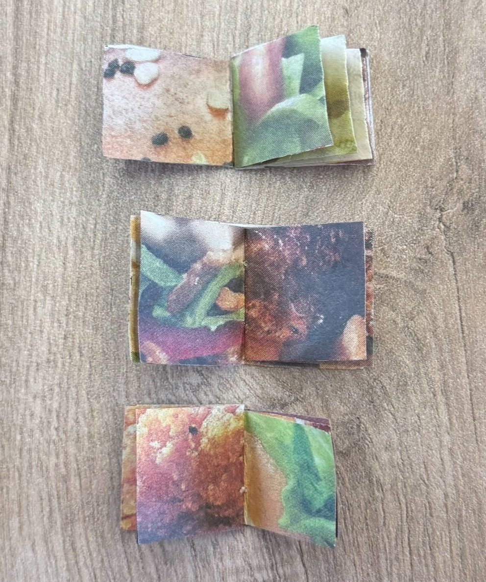 Three small open books, displayed on a table in a vertical line. The first page is a zoomed image of a burger bun next to a zoomed image of lettuce and sauce. The second spread is lettuce and tomato, next to a beef burger patty. The last book shows fried chicken next to lettuce and sauce.