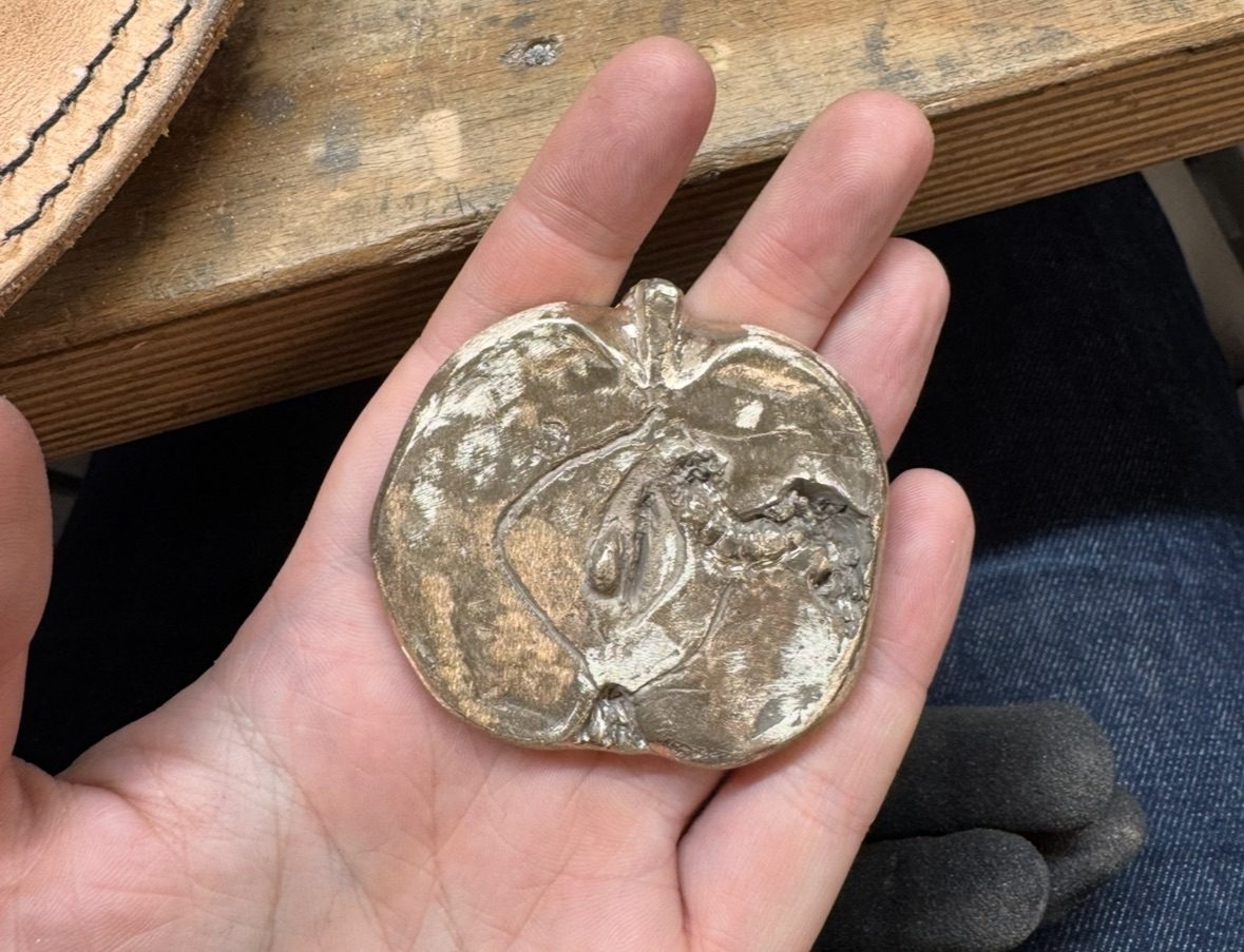 Bronze palm sized sculpture of a cross section of an apple with a maggot in it.