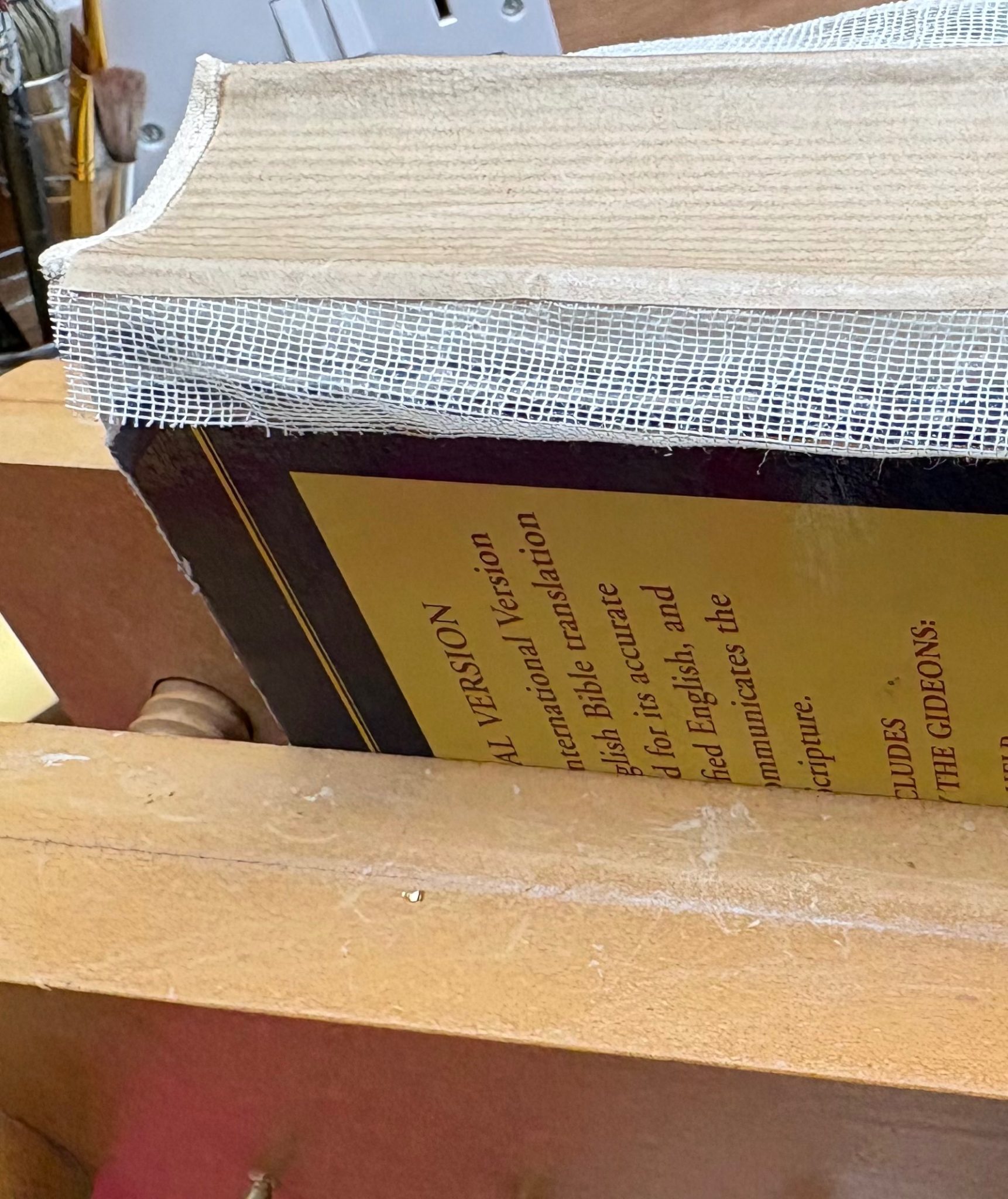 A book block held vertically while its spine is reinforced with paper and gauze prior to making a new binding for it.