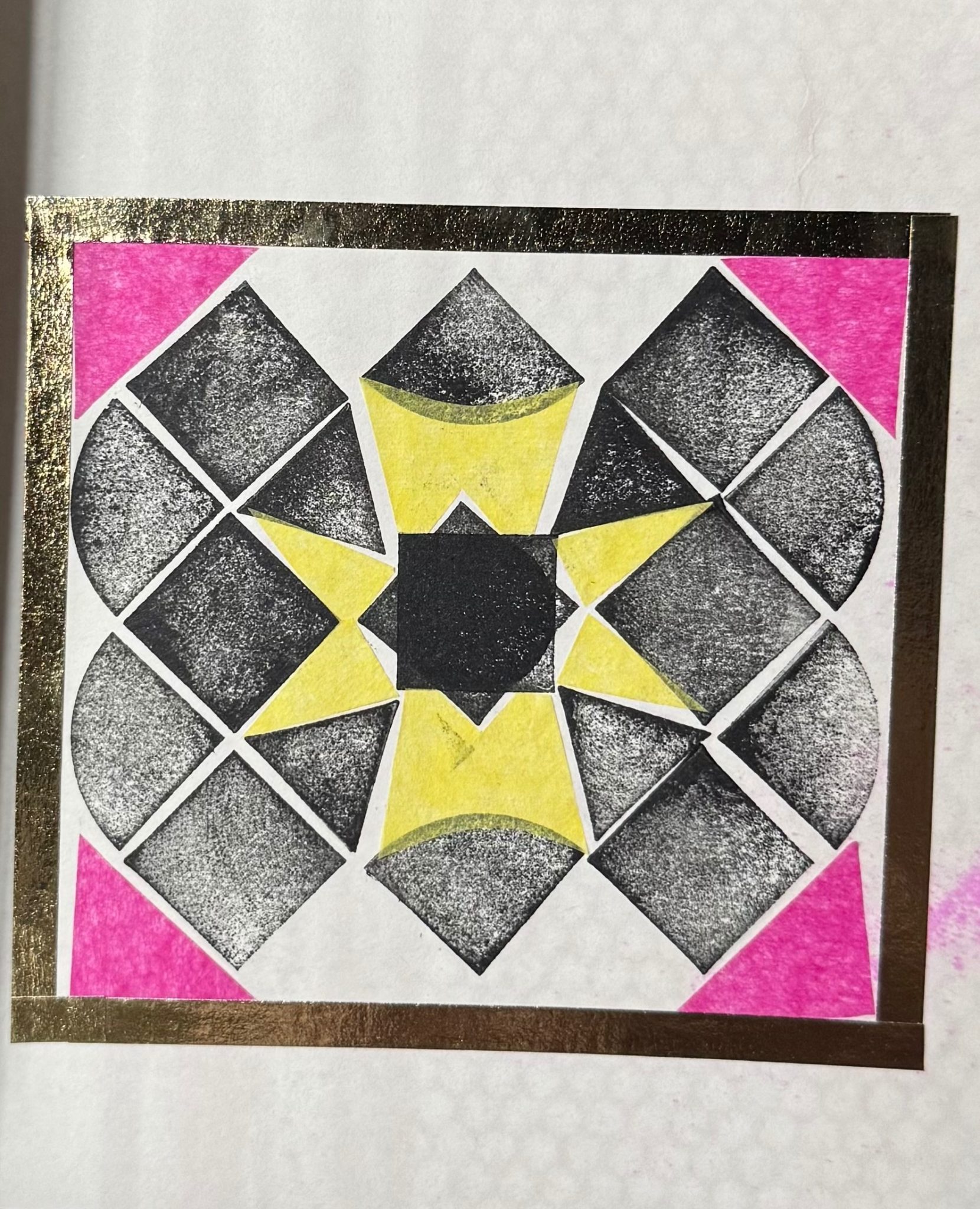 Black and white shapes form a pattern with some pieces of pink and yellow tissue paper. All within a square that is made up of thin gold tape.