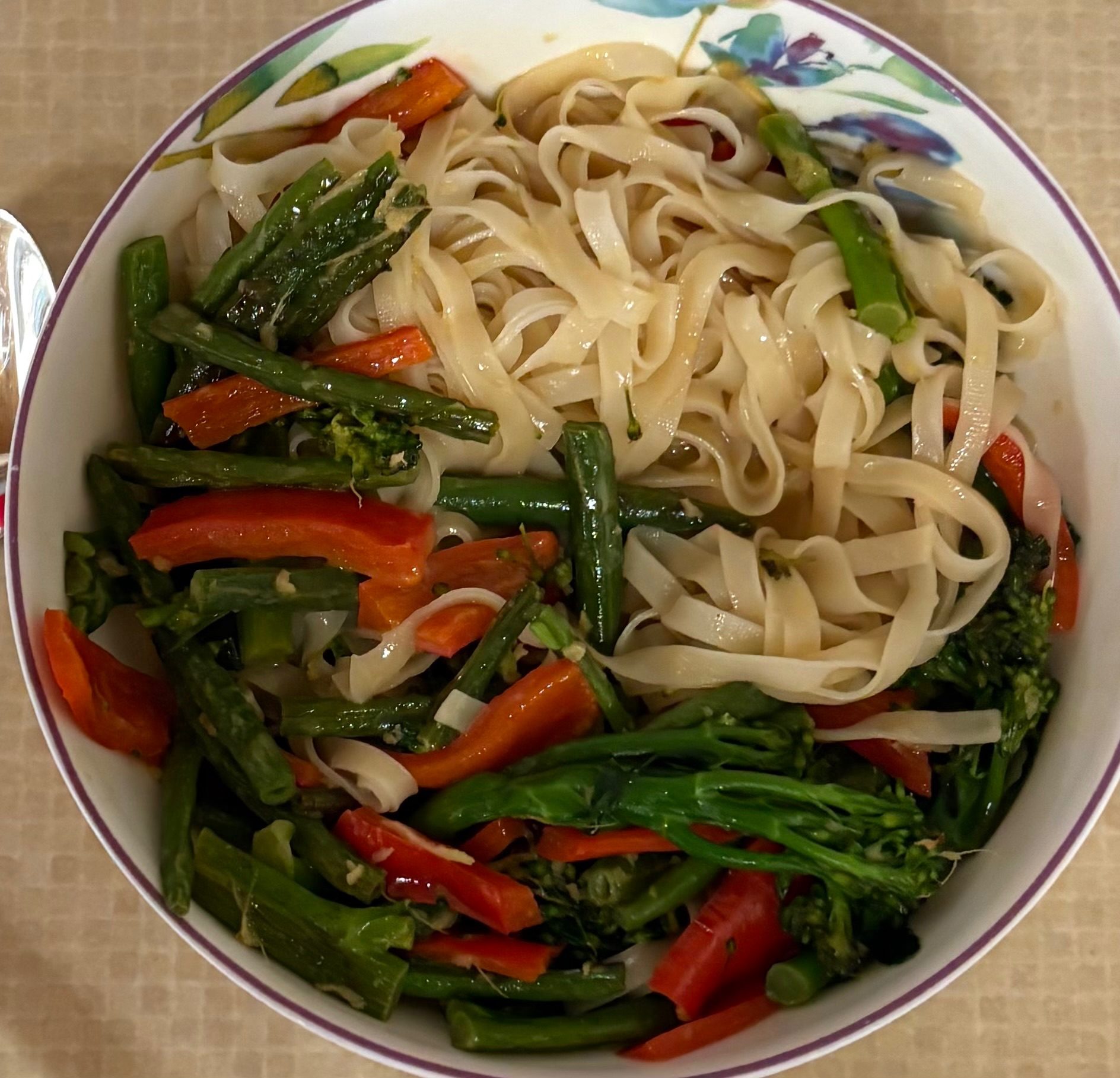 A bowl of rice noodles with red peppers, green beans and purple sprouting broccoli