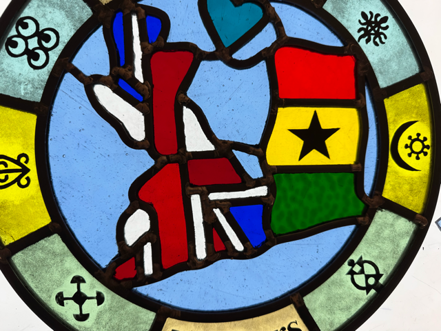 Portion of a glass panel depicting Ghanaian flag with map of UK. Painted around the perimeter are Adinkra symbols.