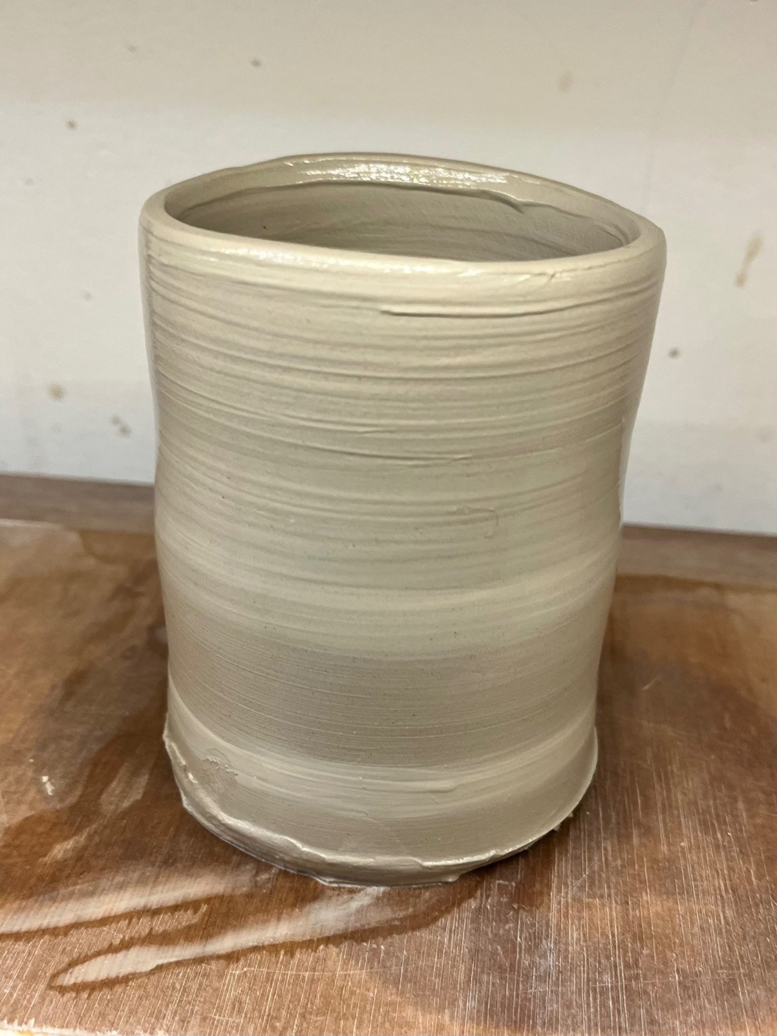 A distorted clay pot dries on a wooden board.
