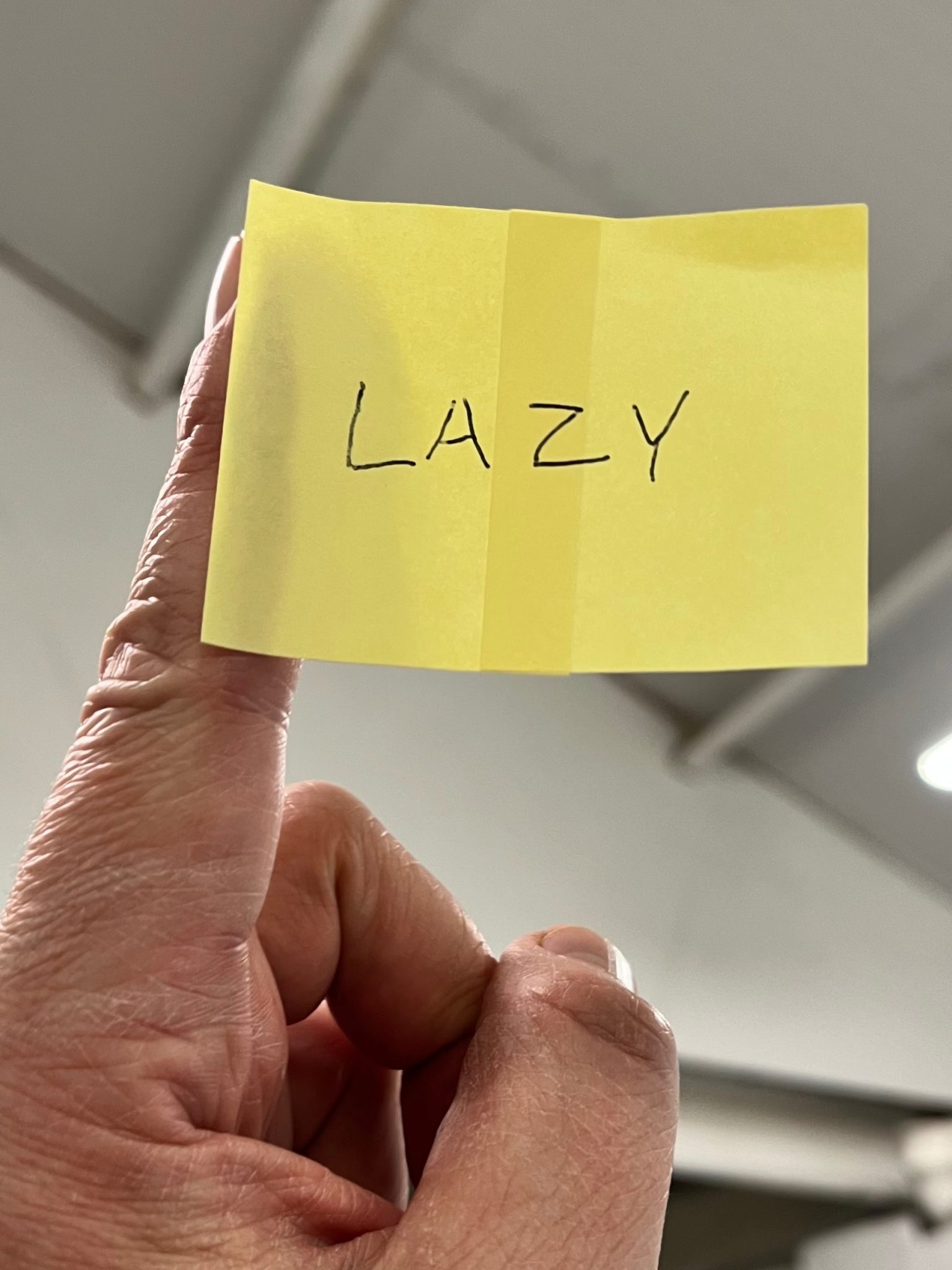 A post-it note flag with the word LAZY written on it. The flag is attached to a finger acting as flagpole.