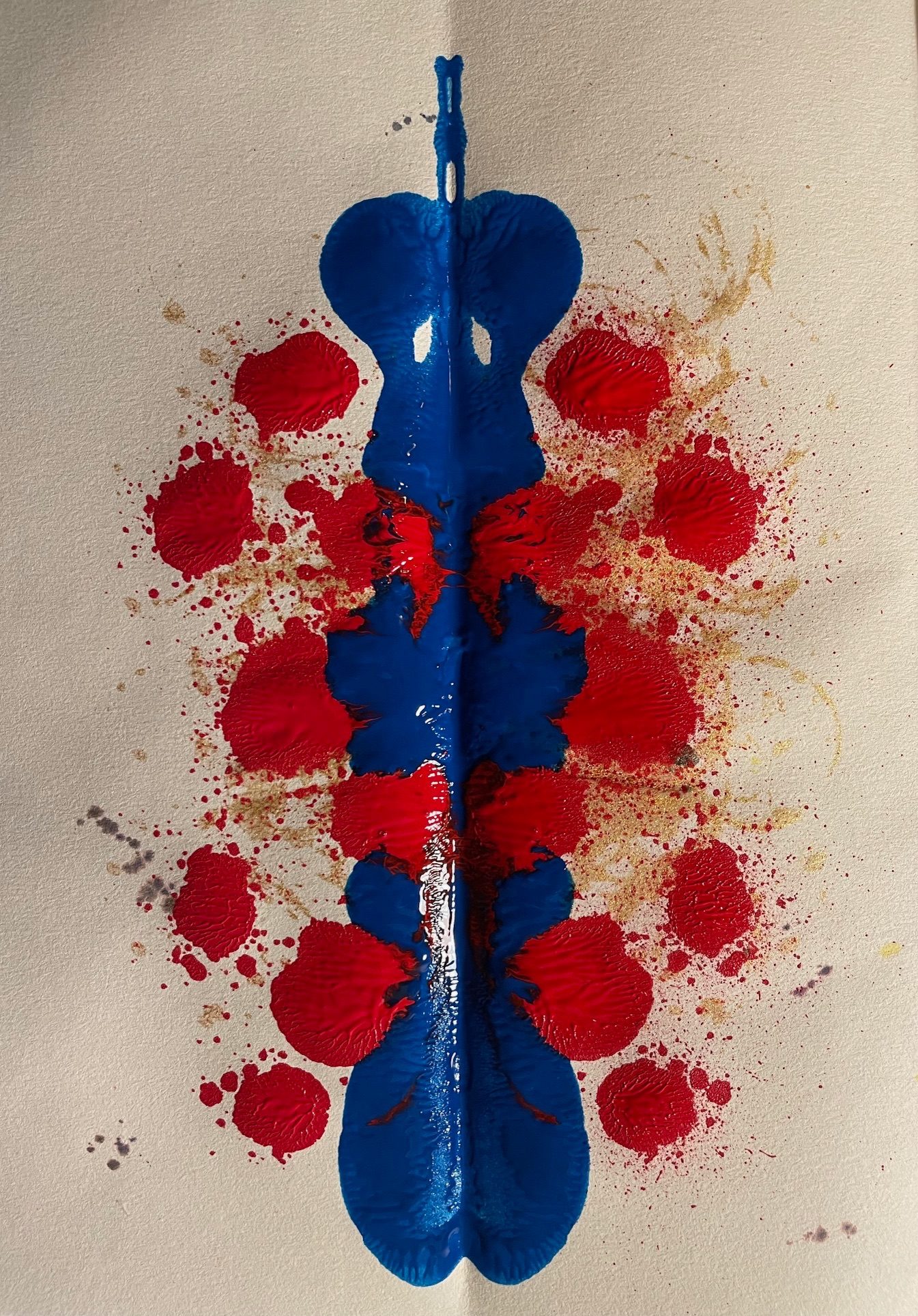 Red, blue and gold paint splats on paper with a vertical line of symmetry