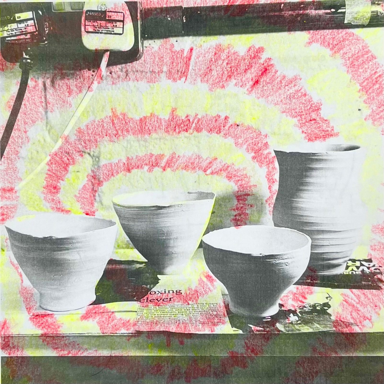 A black and white photo of 4 ceramic objects. One cup has colourful rays of yellow and red crayon radiating from it.