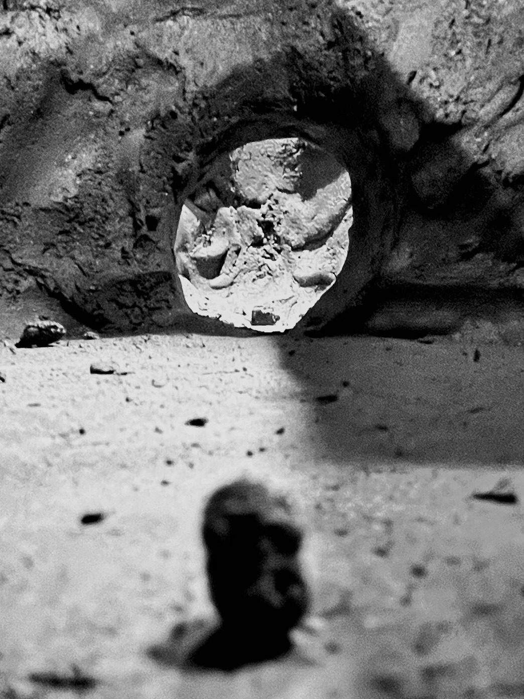 Black and white photo of the inside a kiln. It looks like a cave. A small lump of clay looks like a figure approaching an opening.