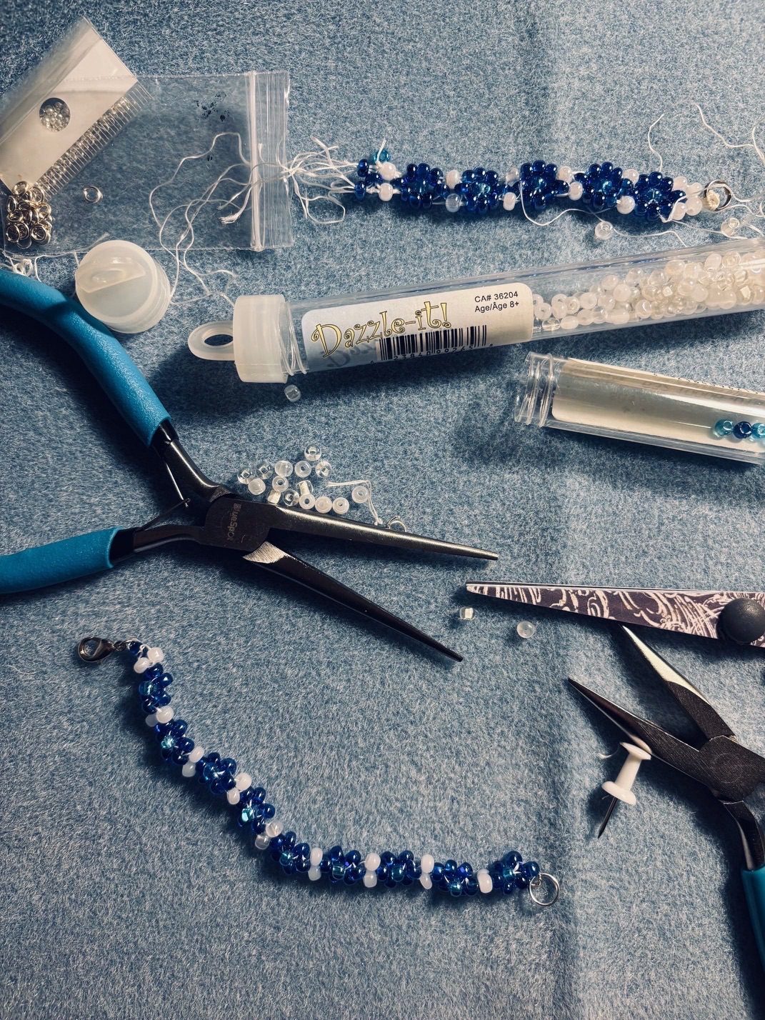 beaded daisy bracelet in blue and white, with scattered tools and materials and the original broken bracelet