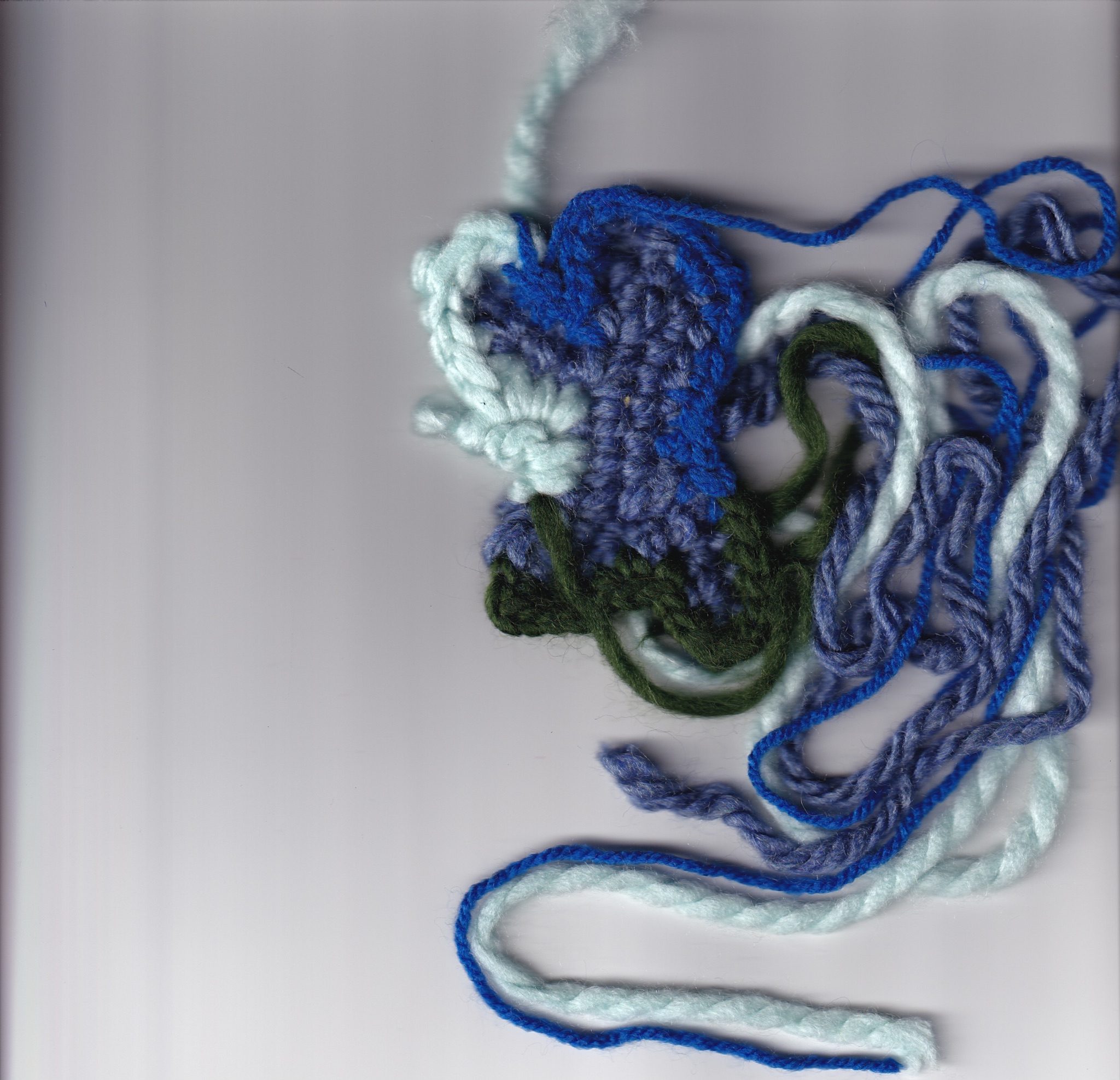 digital scan of a freeform crochet making an abstract, almost butterfly shape in blues and greens with the yarn threads still attached