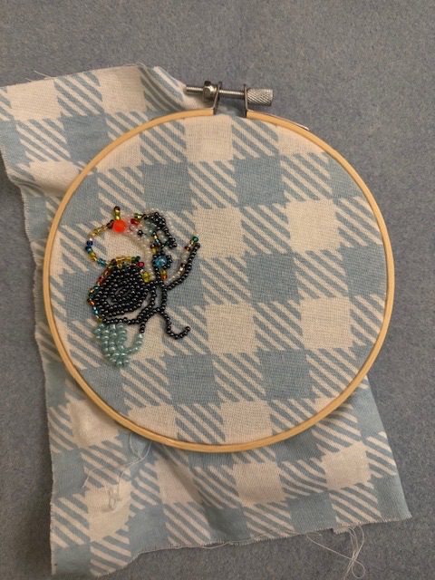 beaded embroidery doodles on plaid fabric in an embroidery hoop