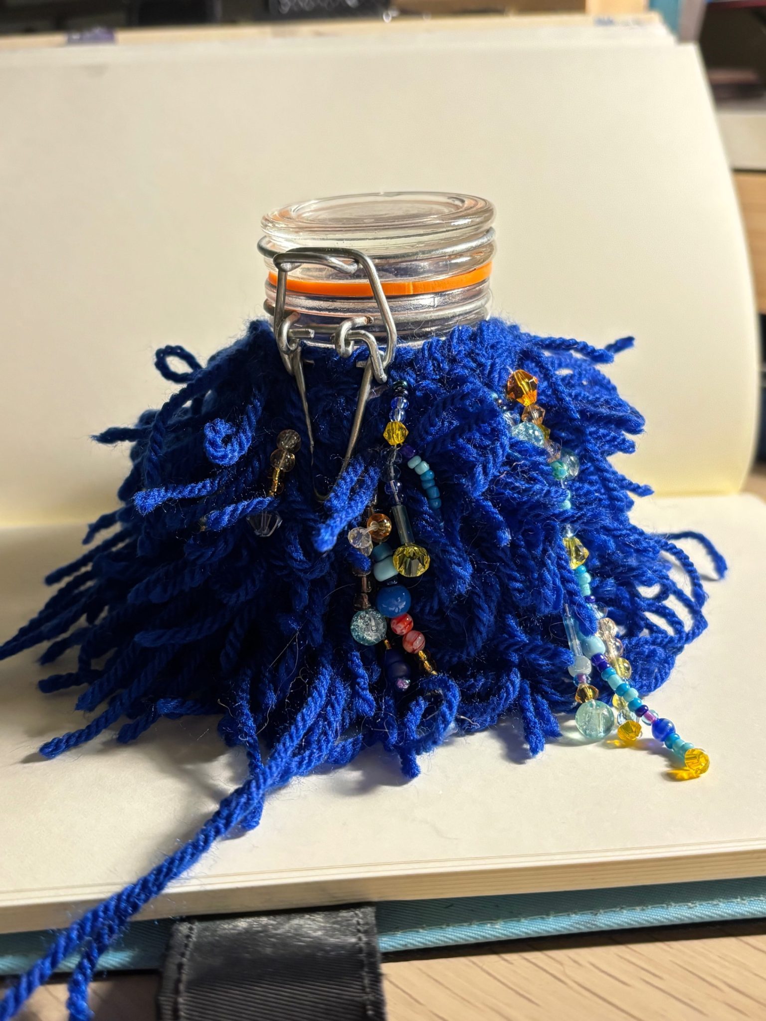 blue shaggy crochet swatch bejewelled with beads wrapped around a small jar